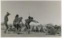 "Daytime Dance at Gautscha 1952, Early in the Dance, approach": Men dancing through a circle of women sitting, with one man's arms outstretched (print is a cropped image)