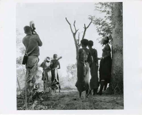 "The 1957-8 Games": Group of women and girls playing Tcxai Djxani (a dancing game) at a tree, with one girl being carried away by other dancers, John Marshall filming them (print is a cropped image)