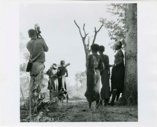 "The 1957-8 Games": Group of women and girls playing Tcxai Djxani (a dancing game) at a tree, with one girl being carried away by other dancers, John Marshall filming them (print is a cropped image)