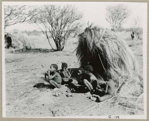 "Auto": Group of children sitting in front of a skerm, with toy cars made of veldkos on the ground next to them (print is a cropped image)