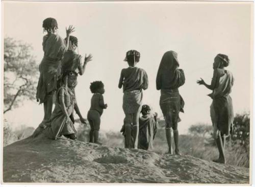 "N!ai on ant hill making patterns, girls playing on ant hill": Children dancing on an ant hill, with girls making patterns in the sand with their feet (print is a cropped image)