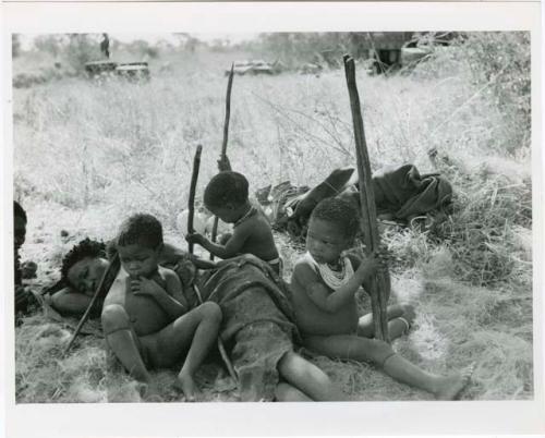 "Children playing, Elizabeth's [Elizabeth Marshall Thomas] 1955 observations": /Naoka (Di!ai's co-wife) lying on the ground, with Bau leaning against her and Debe and /Gaishay holding sticks (print is a cropped image)