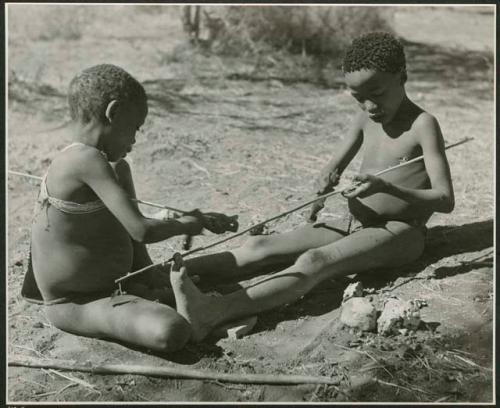 "The Jani [Djani]": Tsamgao (son of ≠Toma), and one of Gau's sons from Band 2 peeling sticks with which to toss the djani (helicopter toy) (print is a cropped image)