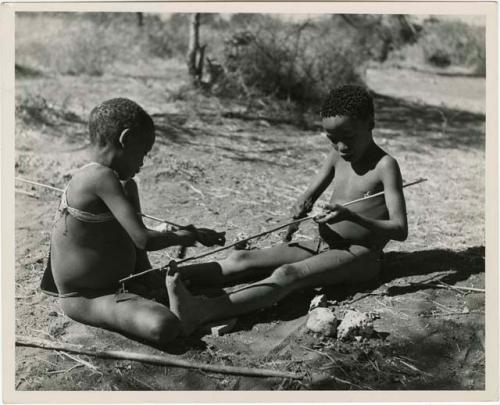 "The Jani [Djani]": Tsamgao (son of ≠Toma), and one of Gau's sons from Band 2 peeling sticks with which to toss the djani (helicopter toy) (print is a cropped image)