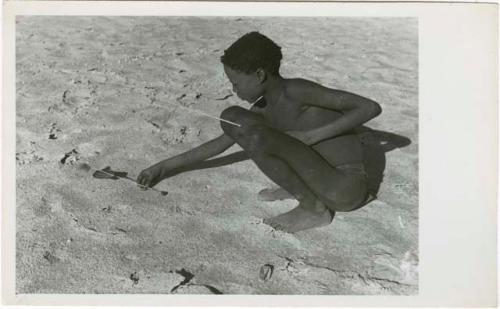 "The Jani [Djani]": Ju/'hoan boy squatting with djani bird (helicopter toy) (print is a cropped image)