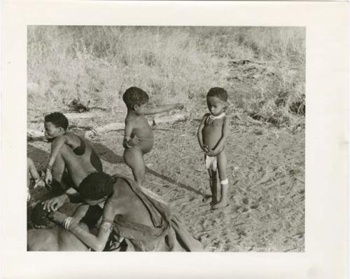 "Photos of Children": !Ungka Norna watching /Gaishay and Bau sharing food, Elizabeth Marshall Thomas taking notes, and other unidentified people; part of Elizabeth Marshall Thomas's child study (print is a cropped image)