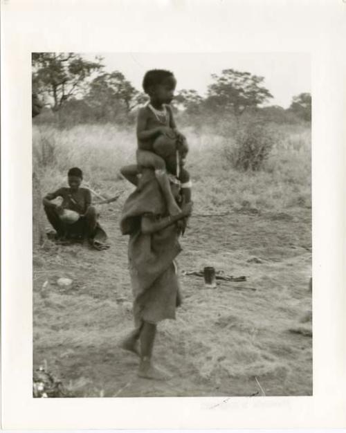 "Photos of Children": Unidentified, visiting girl, standing with !Ungka Norna on her shoulders (print is a cropped image)