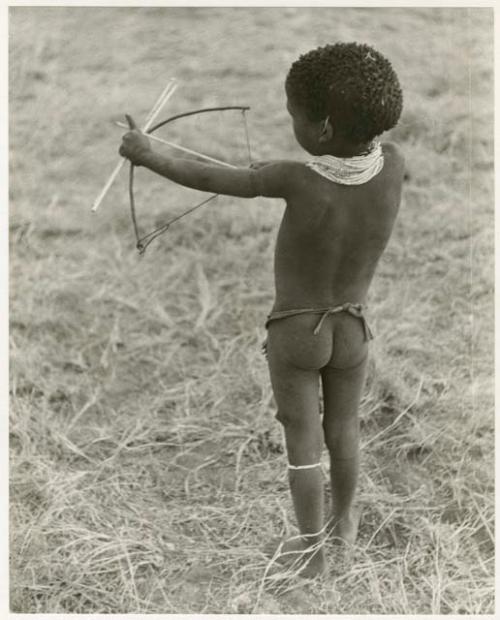 /Gaishay ("Gao Medicine" and Di!ai's son) with a toy bow and arrow, pulling back the string to release an arrow, view from behind (print is a cropped image)
