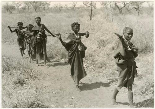 Girls walking in a line including an unidentified, visiting girl in the front, another unidentified girl, !Ungka's cousin, and several younger girls (print is a cropped image)

