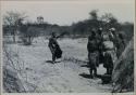 Group of women standing by a skerm; !Xoa standing with her arm up in the background



