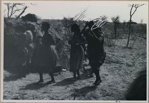 Group of people performing the Eland Dance; group of women clapping; men holding wooden horns to their heads



