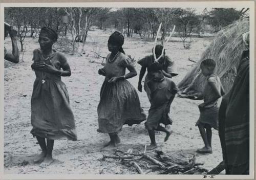 Group of people performing the Eland Dance; a line of people, men holding wooden horns to their heads



