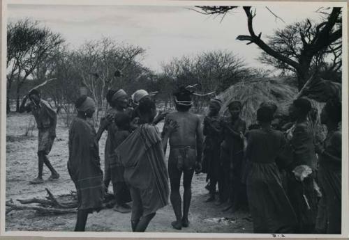 Group of people performing the Eland Dance; group of women clapping; men with wooden horns on their heads



