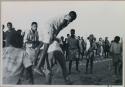 Boy leaping over another boy, people watching in the school yard



