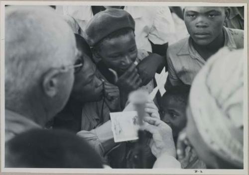 Laurence Marshall showing polaroid photographs to a group of people, close-up view




