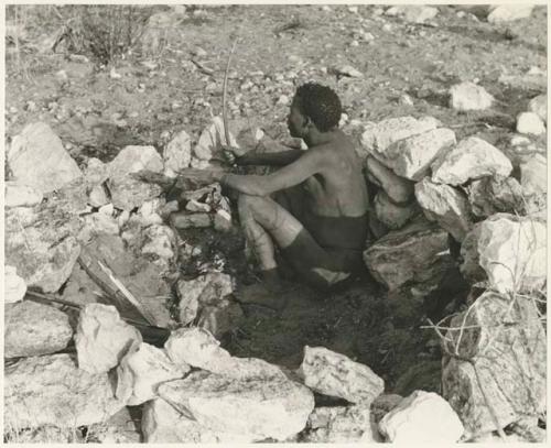 "Crooked /Qui" squatting in a hunting blind built of stone (print is a cropped image)