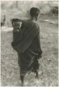 Woman walking with a baby in her kaross, seen from the back (print is a cropped image)