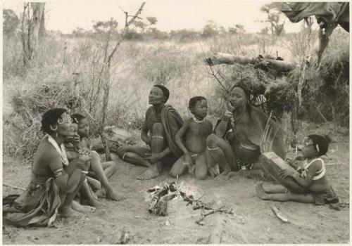 Gao and Di!ai with two children sitting beside fire; unidentified woman and children to the left (print is a cropped image)