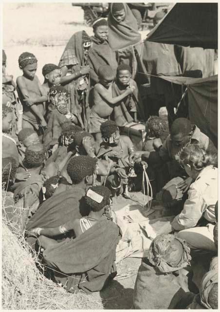 Group of Ju/'hoansi, Kernel Ledimo, and Lorna Marshall gathered around to look at beads (print is a cropped image)