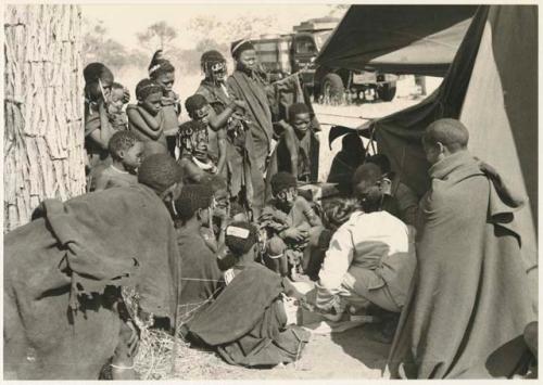 Group of Ju/'hoansi, Kernel Ledimo, Lorna Marshall gathered around to look at beads, seemingly in the cold (print is a cropped image)