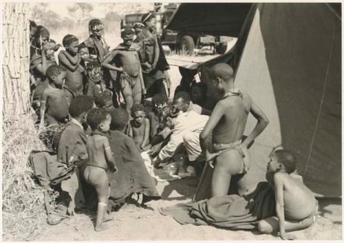 Group of Ju/'hoansi, Kernel Ledimo, and Lorna Marshall gathered around to look at beads, seemingly in the cold (print is a cropped image)