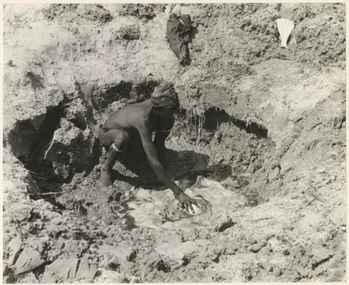 "/Gao Music" squatting to fill an ostrich eggshell in a waterhole (print is a cropped image)