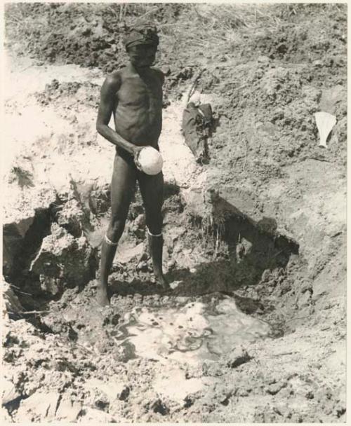 "/Gao Music" standing beside a waterhole with an ostrich eggshell (print is a cropped image)