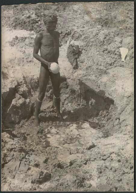 "/Gao Music" standing beside a waterhole with an ostrich eggshell (print is a cropped image)