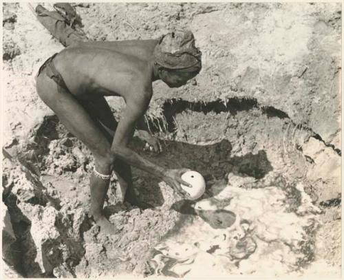 "/Gao Music" dipping an ostrich eggshell in a waterhole (print is a cropped image)