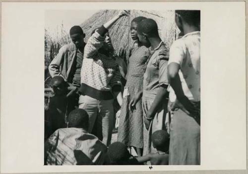 Girl having her height measured by Deborah Marshall, and other people standing next to them (print is a cropped image)