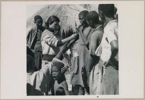 Girl having her height measured by Deborah Marshall, and other people standing near them (print is a cropped image)