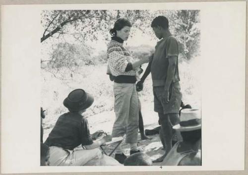 Man having his skin color documented by Deborah Marshall, and Lorna Marshall taking notes (print is a cropped image)