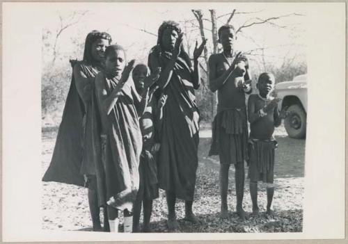 Group of women and children clapping and singing (print is a cropped image)