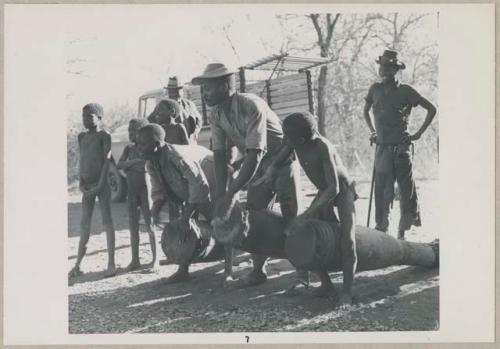 Two men and a boy playing drums, with other people standing nearby (print is a cropped image)