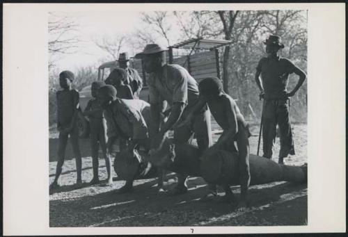 Two men and a boy playing drums, with other people standing nearby (print is a cropped image)