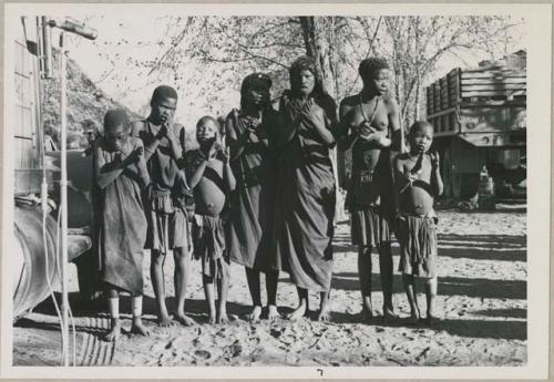 Group of women and children singing, with expedition truck in background (print is a cropped image)