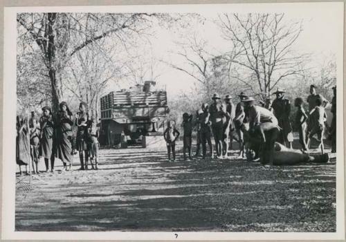 Men playing drums, and group of people singing, with expedition truck in background (print is a cropped image)