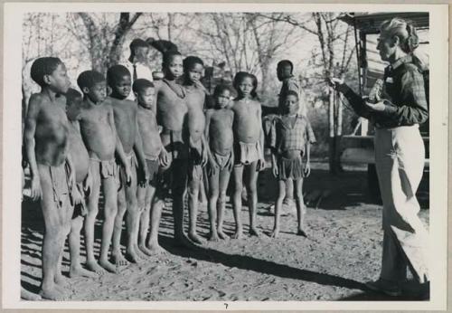 Group of children standing, and Lorna Marshall taking a light reading (print is a cropped image)