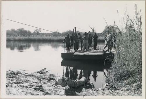 Group of people standing on a float that is crossing the water (print is a cropped image)