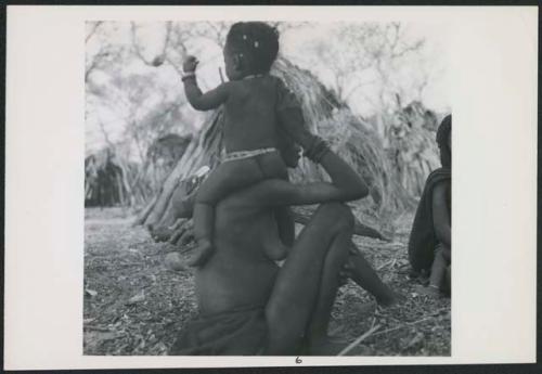 Woman sitting and holding a baby on her shoulder (print is a cropped image)