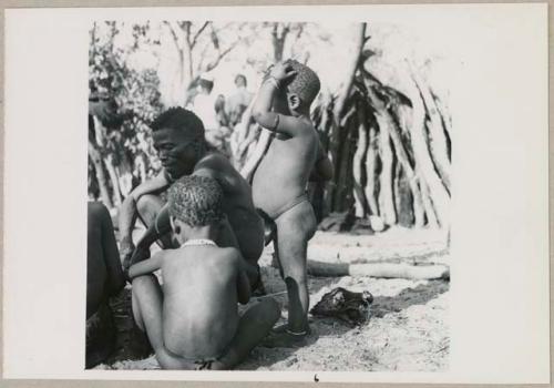 Kumsa sitting, with children sitting and standing next to him (print is a cropped image; image is flipped)