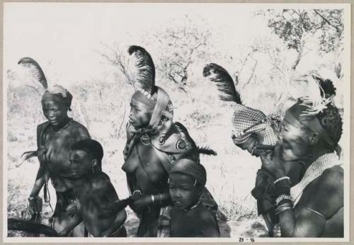 Group of six people standing together with feathers in their hair (print is a cropped image)