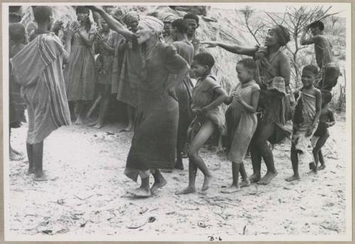 N//aba leading a group of girls, /Gishay holding eland horns in the background (print is a cropped image)