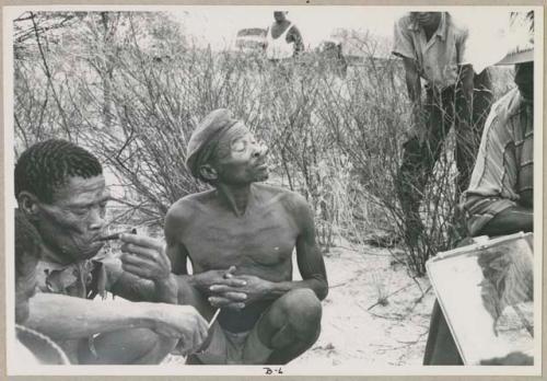 Wilhelm Camm in a chair with a sound recorder interviewing two men sitting on the ground (print is a cropped image)