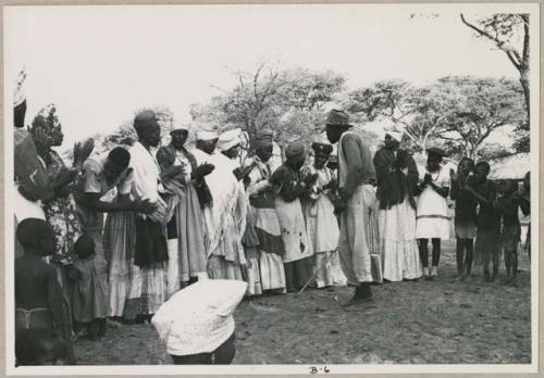 Women standing in a line singing with Judas Kangengi standing in the middle (print is a cropped image)