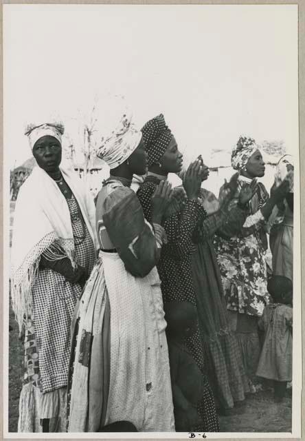 Women standing in a line, clapping (print is a cropped image)