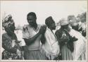 Ananias standing in a line with women who are clapping (print is a cropped image)