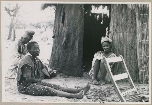 Three women sitting in front of a hut (print is a cropped image)