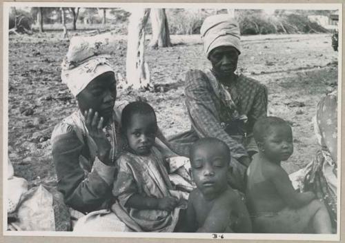 Two women seated, child sitting in one woman's lap, two children sitting in front of them (print is a cropped image)