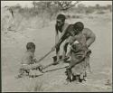 "Pulling on Kaross / Pulling on Gemsbok Horns / Carrying on Kaross "Airplane".": Tsamgao (≠Toma's son) and an unidentified boy pulling /Qui (son of Khuan//a) on gemsbok horns, with Be watching them (print is a cropped image)